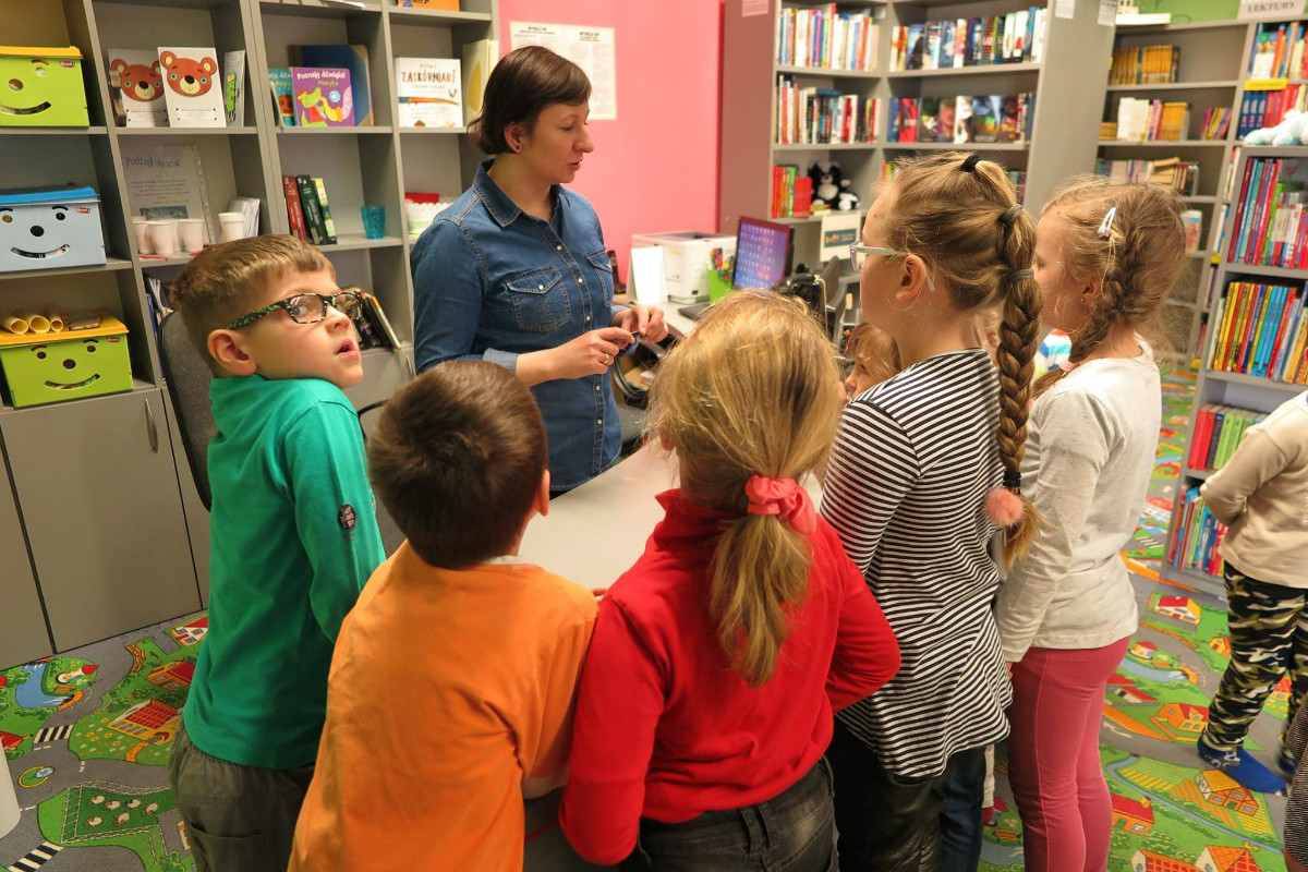 Przy biurku stoi grupa dzieci i bibliotekarka Ania Wiśniewska.