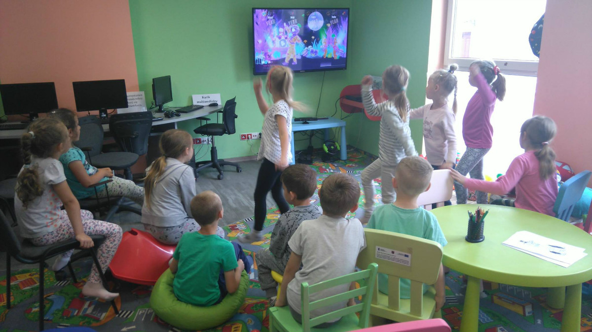 Dzieci tańczą do wyświetlonej prezentacji na telewizorze. 