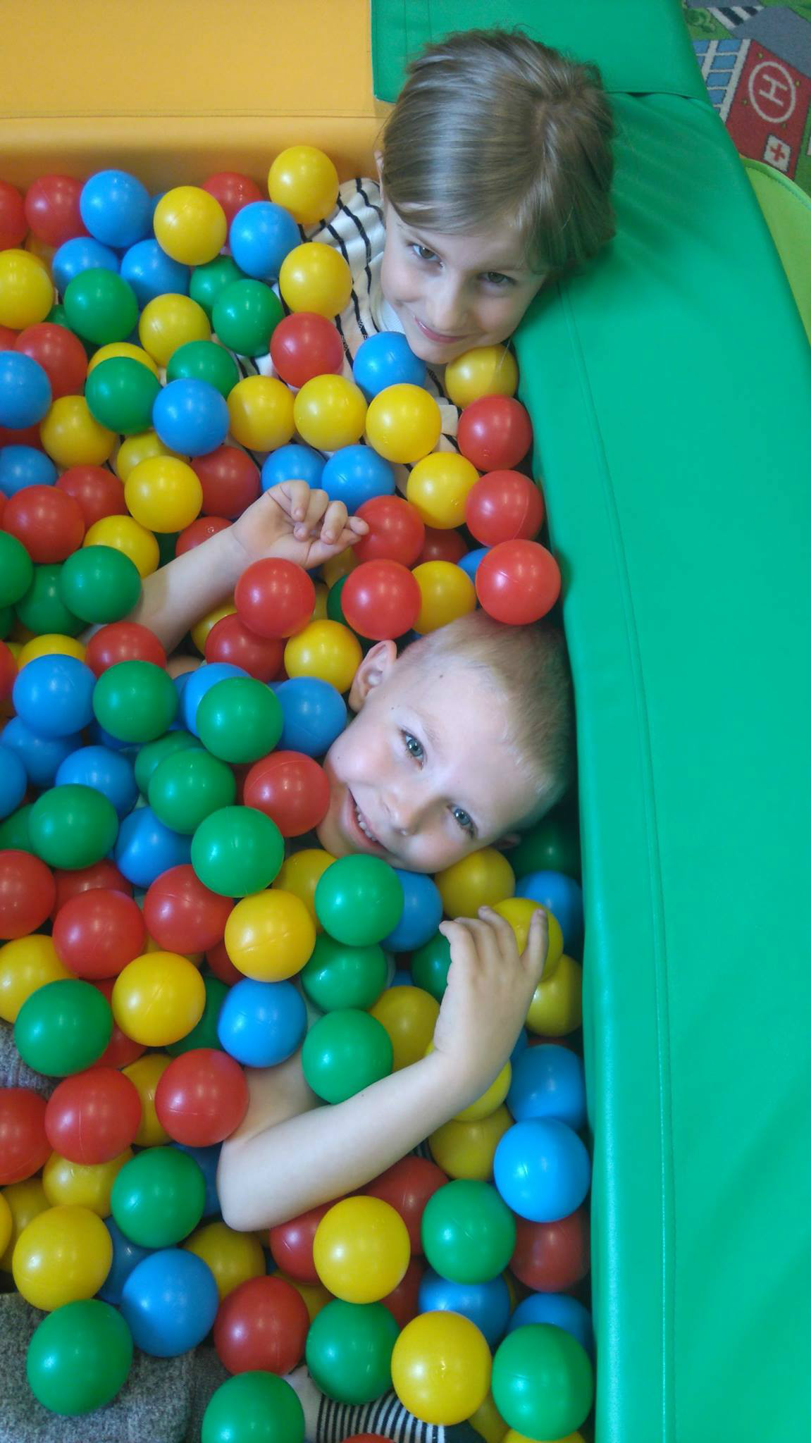 W basenie z kolorowymi piłeczkami bawi się chłopczyk z dziewczynką. 