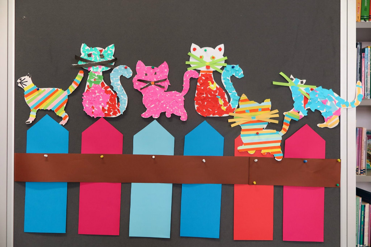 Wnętrze biblioteki. Na tablicy wisi kolorowy płot i kotki wycięte z kolorowego papieru przez dzieci z Klubu Malucha. 