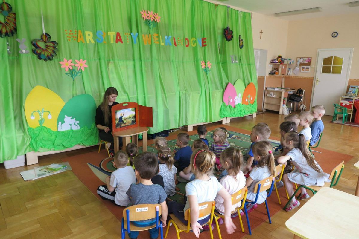 Wnętrze Przedszkola nr 1 , grupa dzieci słucha teatrzyku kamishibai. 