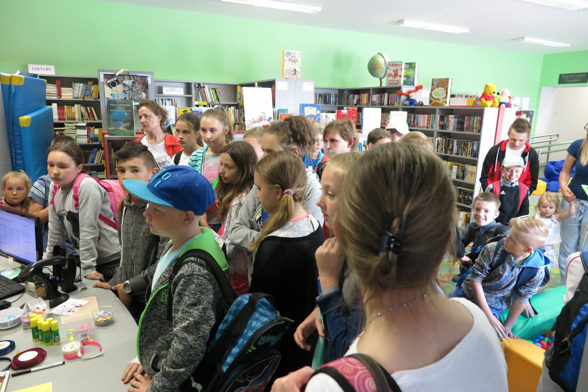 Wnętrze biblioteki. Grupa uczniów ze SP w Petrykozach zwiedza oddział dla dzieci. 