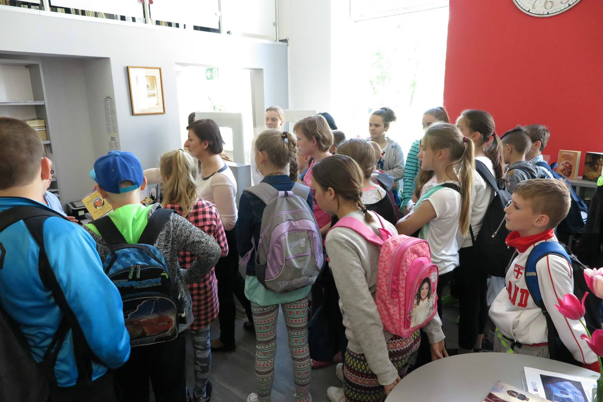 Wnętrze biblioteki. Grupa uczniów ze SP w Petrykozach zwiedza oddział dla dorosłych.