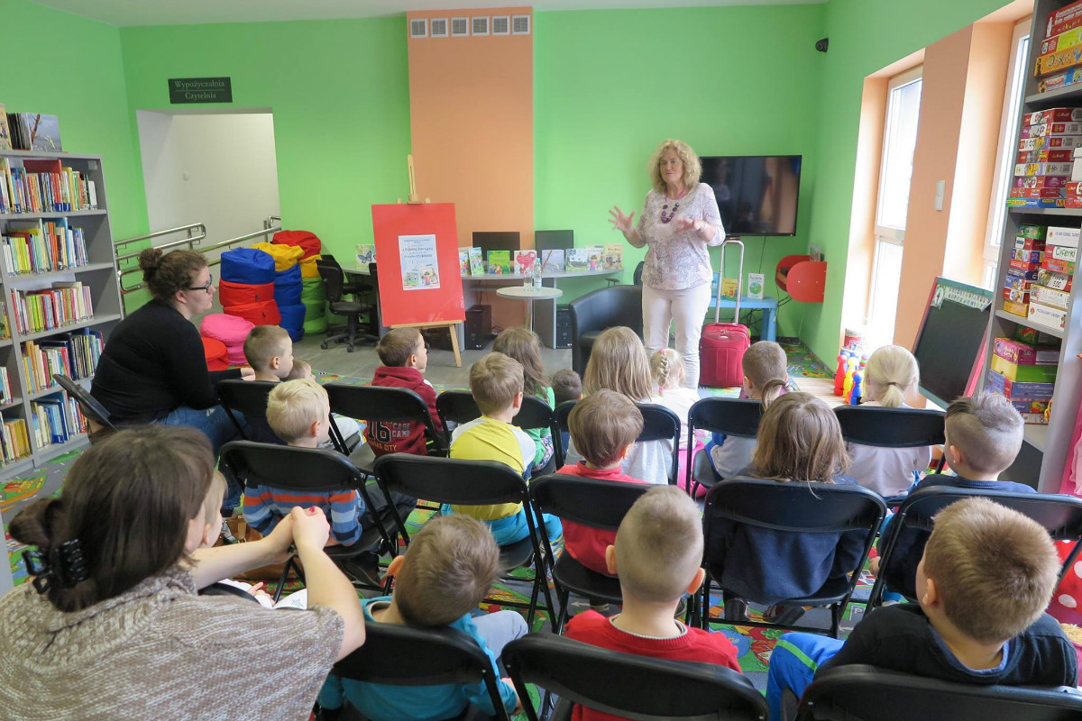 Wnętrze biblioteki. Na krzesełkach siedzą dzieci ze SP nr.4 biorą udział w zajęciach  z autorką książek Elżbietą Zubrzycką.
