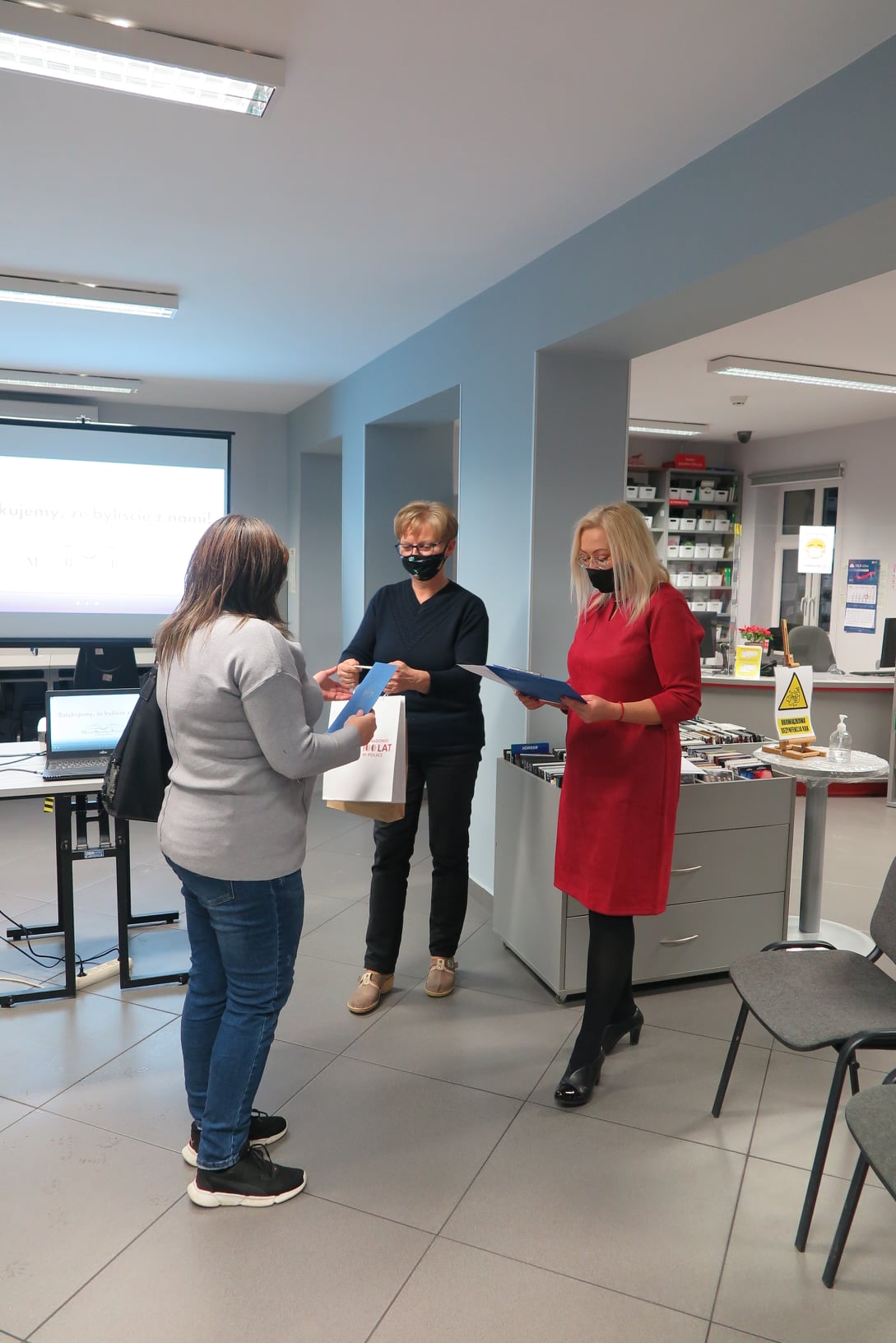 Wnętrze biblioteki mediateka. Dyrektor biblioteki Justyna Lytvyn wraz z kustoszem Elżbietą Wojcieszak wręczają nagrodę laureatce. 