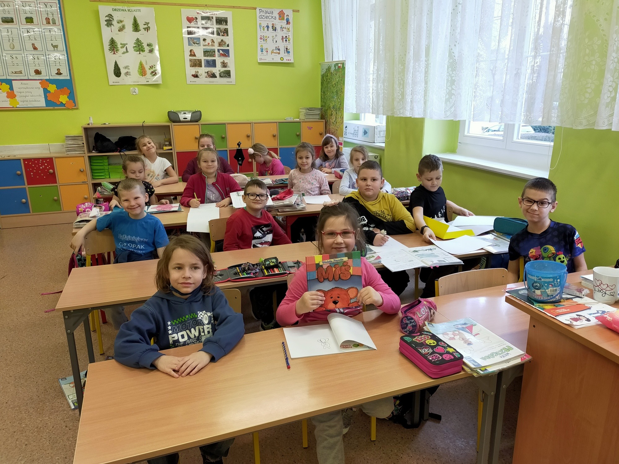 Wnętrze klasy, dzieci siedziące w ławkach omawiające książkę Wioletty Piaseckiej ''MIŚ''