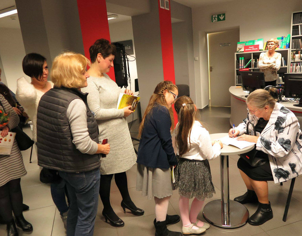 Przy stoliku Anna Kazimiera Cegiełka podpisuje swój tomik dla młodej czytelniczki.