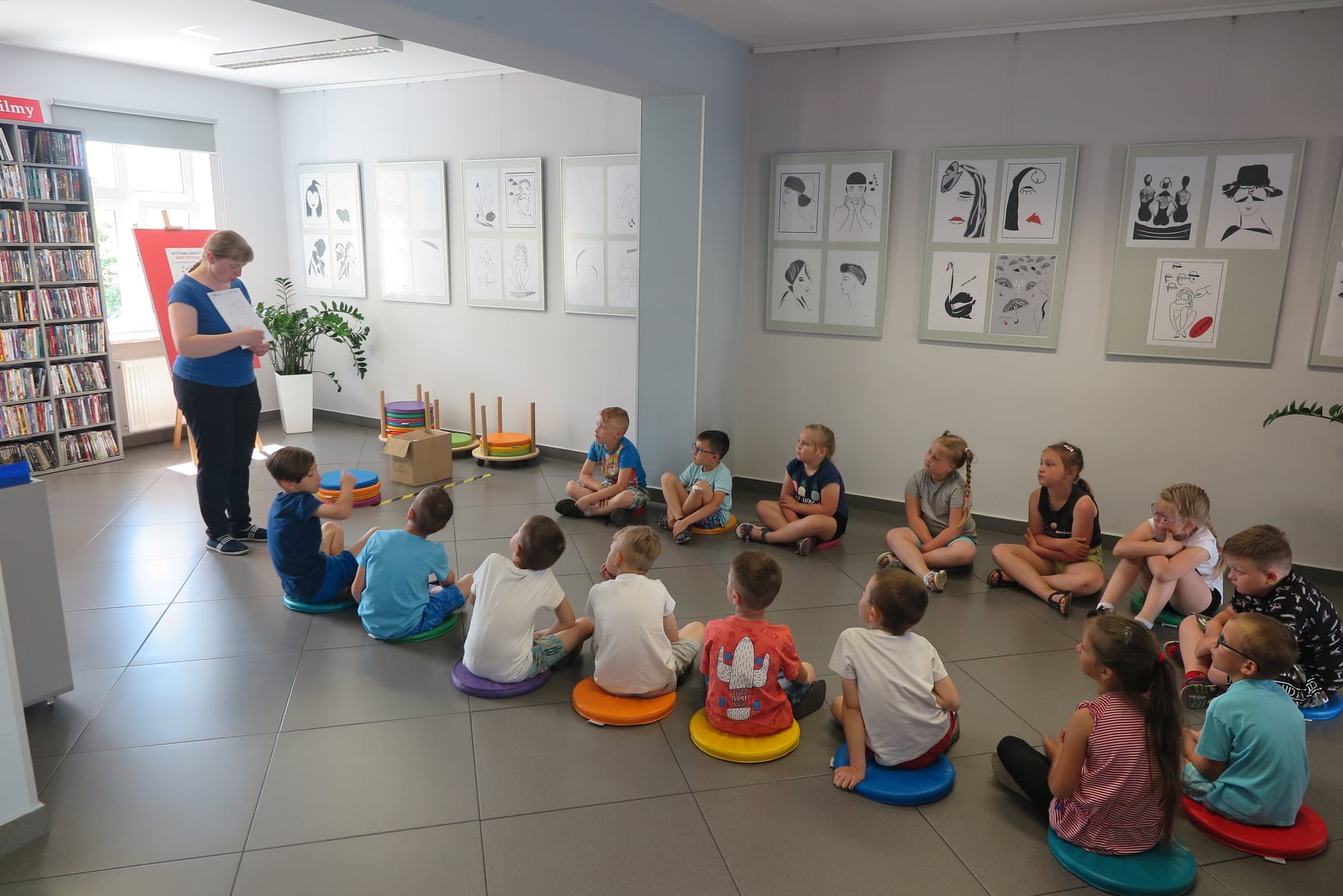 dzieci siedzą na podłodze w mediatece, bibliotekarka tłumaczy im jak działa ozobot