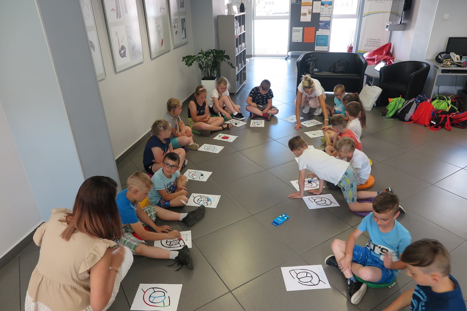 Dzieci siedzą na podłodze na matach w Mediatece, przed nimi kartki formatu a4 z narysowaną trasą dla ozobaota