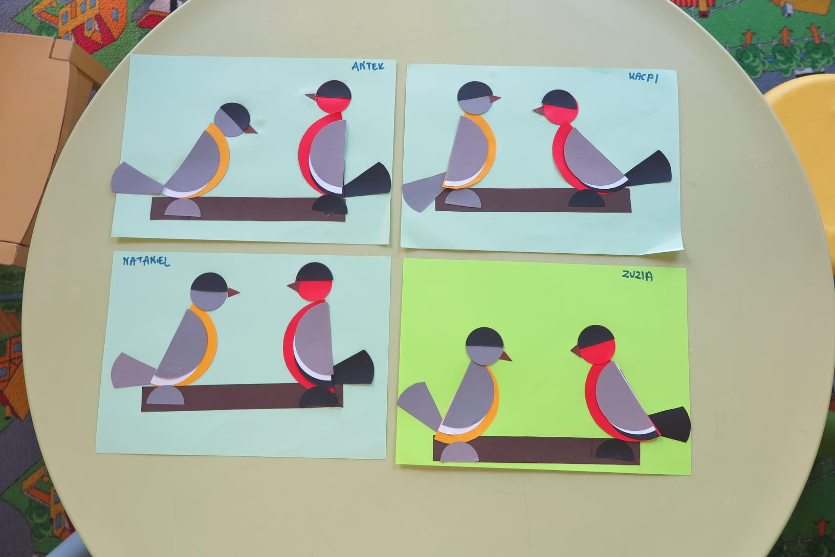 Na zdjęciu cztery kartki papieru. Na każdej wyklejone są dwa kolorowe ptaszki siedzące na gałęzi. Podpisy na każdej kartce: "Antek", "Kacpi", "Nataniel", "Zuzia".