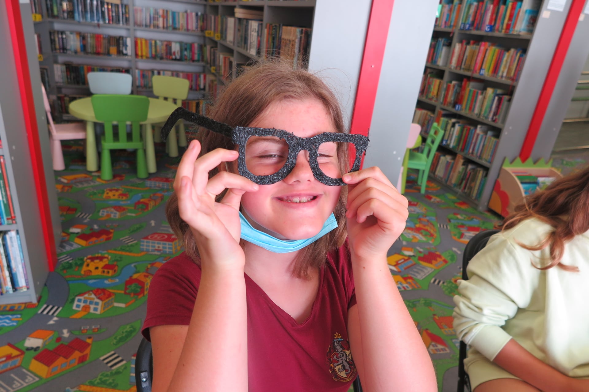 Na zdjęciu dziewczynka, przykładająca do oczu czarne okulary wykonane za pomocą długopisu 3D.