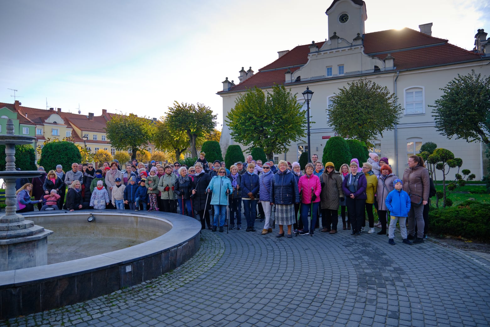 Rynek miasta Działdowo, z lewej fontanna, za nią grupa ludzi pozująca do grupowego zdjęcia, w tle ratusz miasta i kamienice 