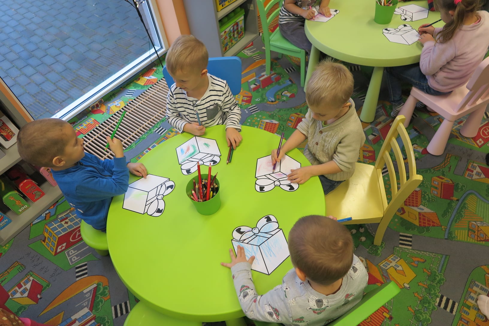 4 chłopców siedzi przy małym stoliku i koloruje kredkami prezenty z papieru