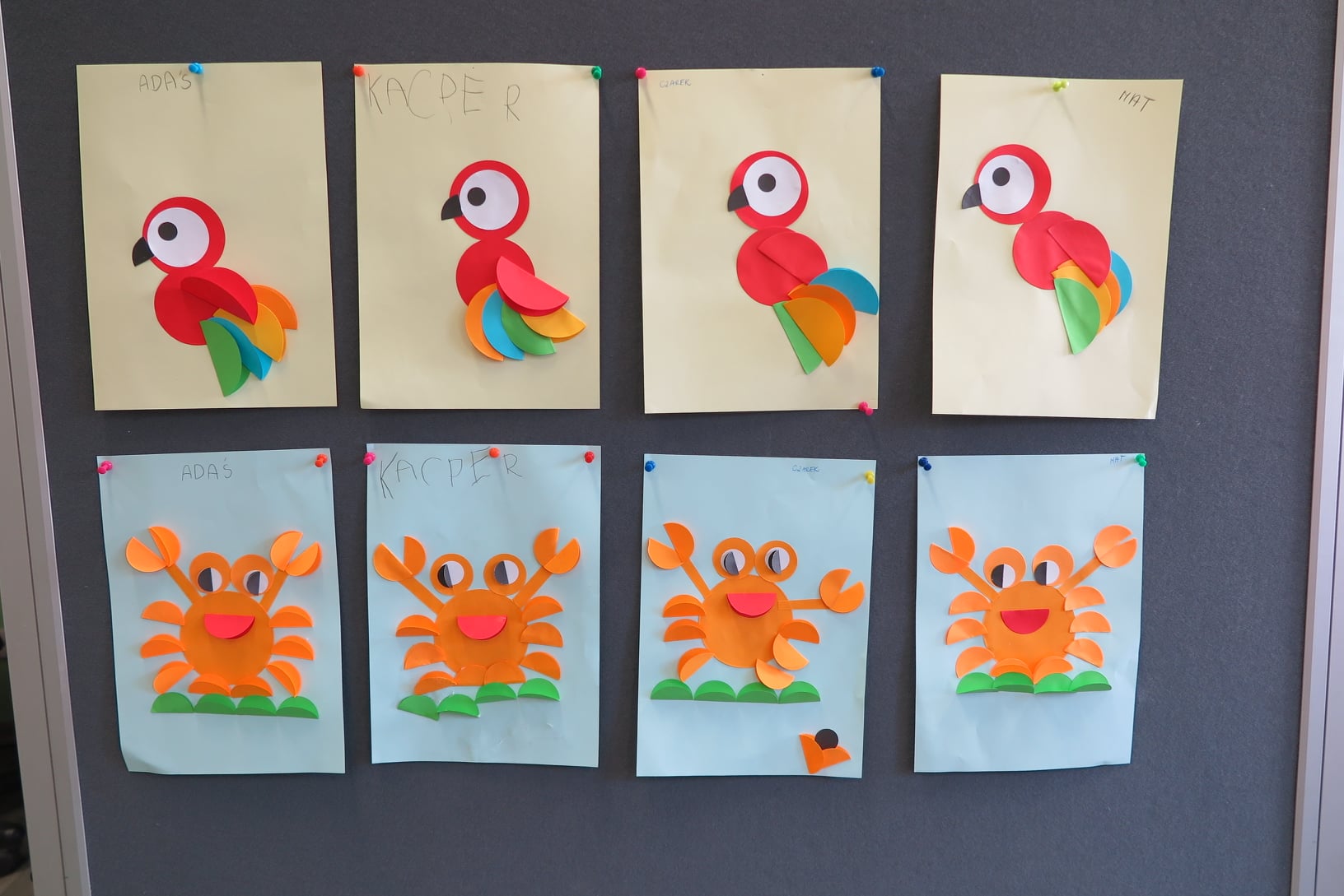 prace wykonane przez dzieci wywieszone na tablicy (wycinanki papugi i kraba)