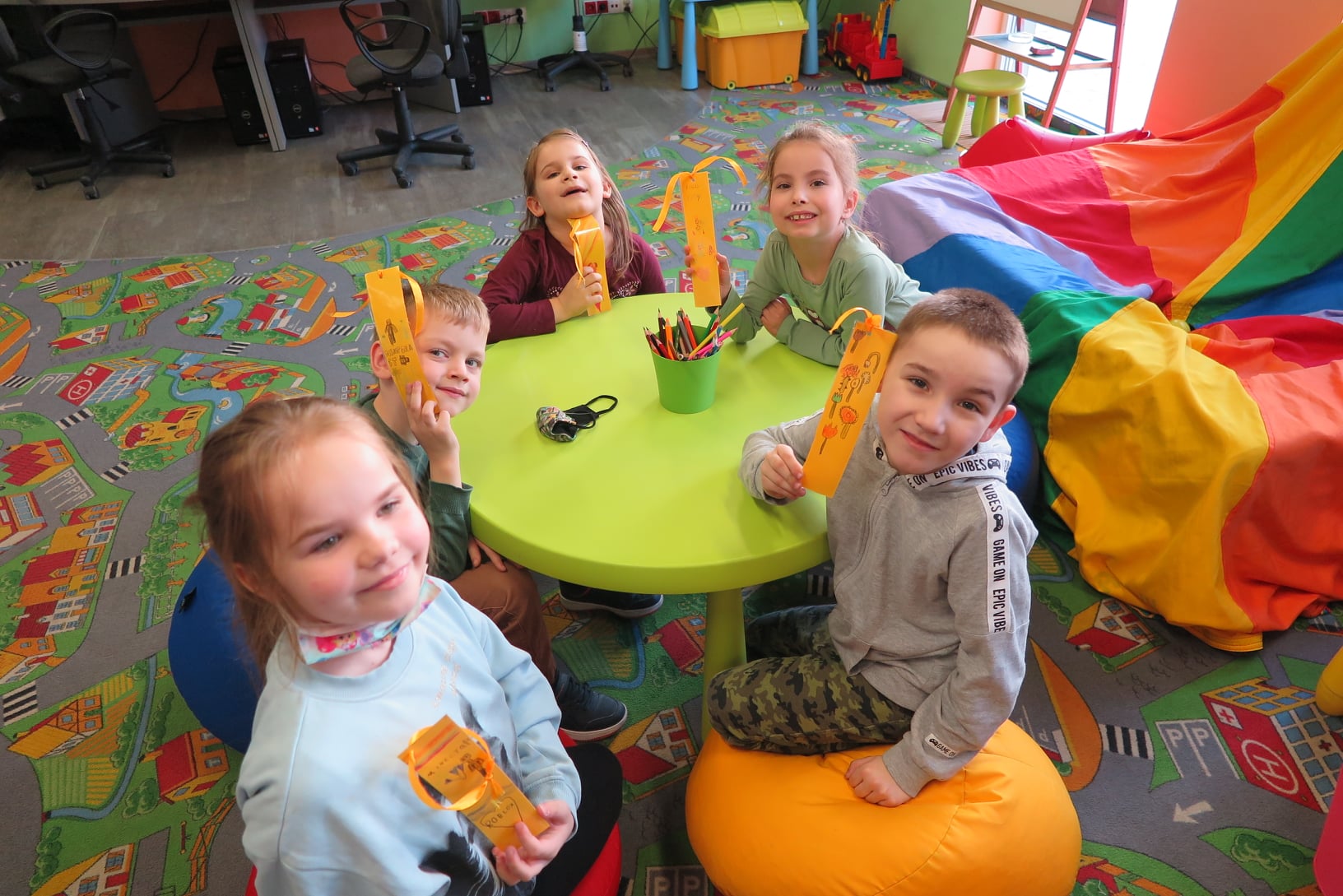 dzieci siedzą przy okrągłym stoliku, pokazują wykonane na zajęciach zakładki do książek
