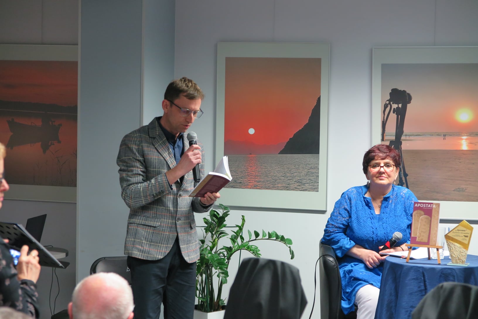 Piotr Kozikowski czyta fragment książki, Krystyny Sztramskiej która siedzi po prawej stronie sceny