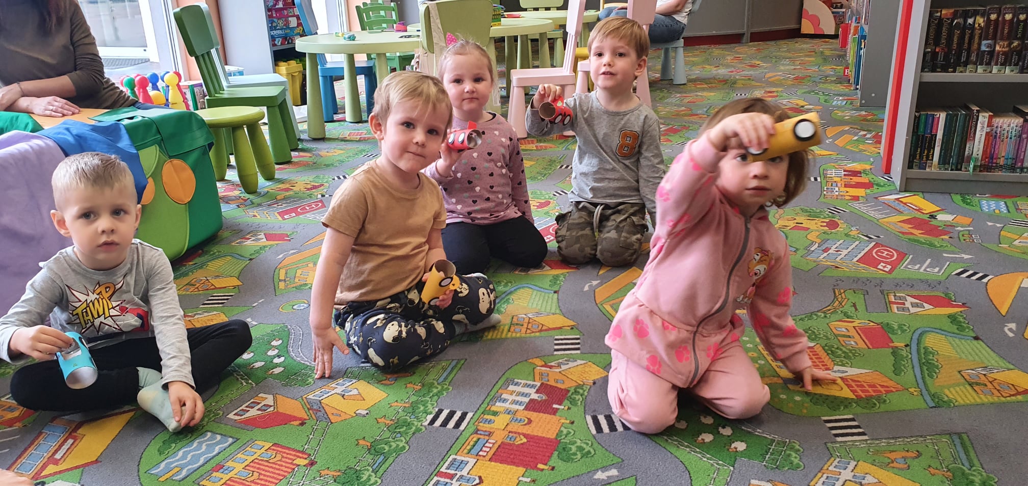 dzieci siedzą na dywanie w oddziale dla dzieci , w rękach trzymają wykonane z rolek po papierze samochody