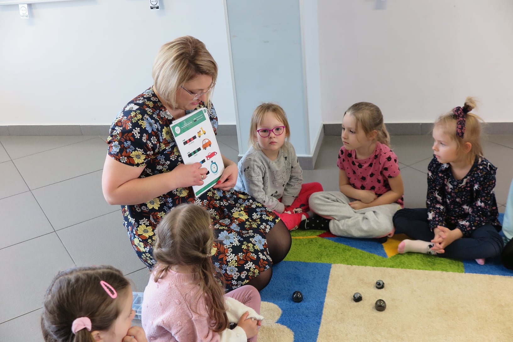 bibliotekarka tłumaczy dzieciom siedzącym na dywanie w mediatece jak programować ozobota
