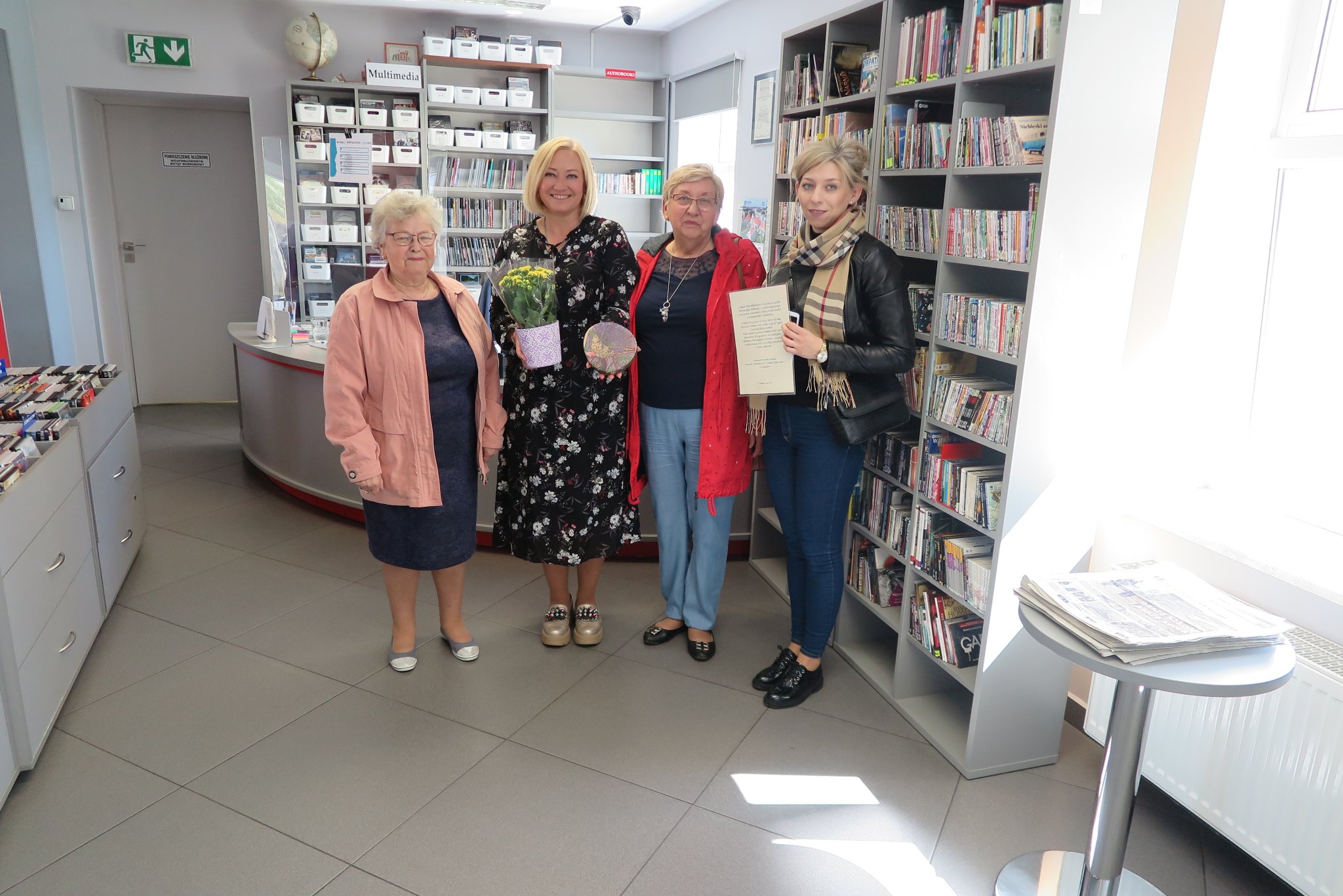 4 kobiety, dyrektor biblioteki i 3 kobiety z klubu seniora wręczają dyrektorce prezent z okazji dnia bibliotekarza i bliblioteki