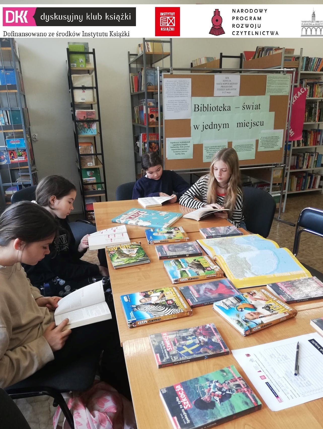 uczniowie w bibliotece szkolnej podczas spotkania klubowego DKK, na stolikach leżą książki, uczniowie siedzą na krzesłach przy stoliku, w tle regały biblioteczne