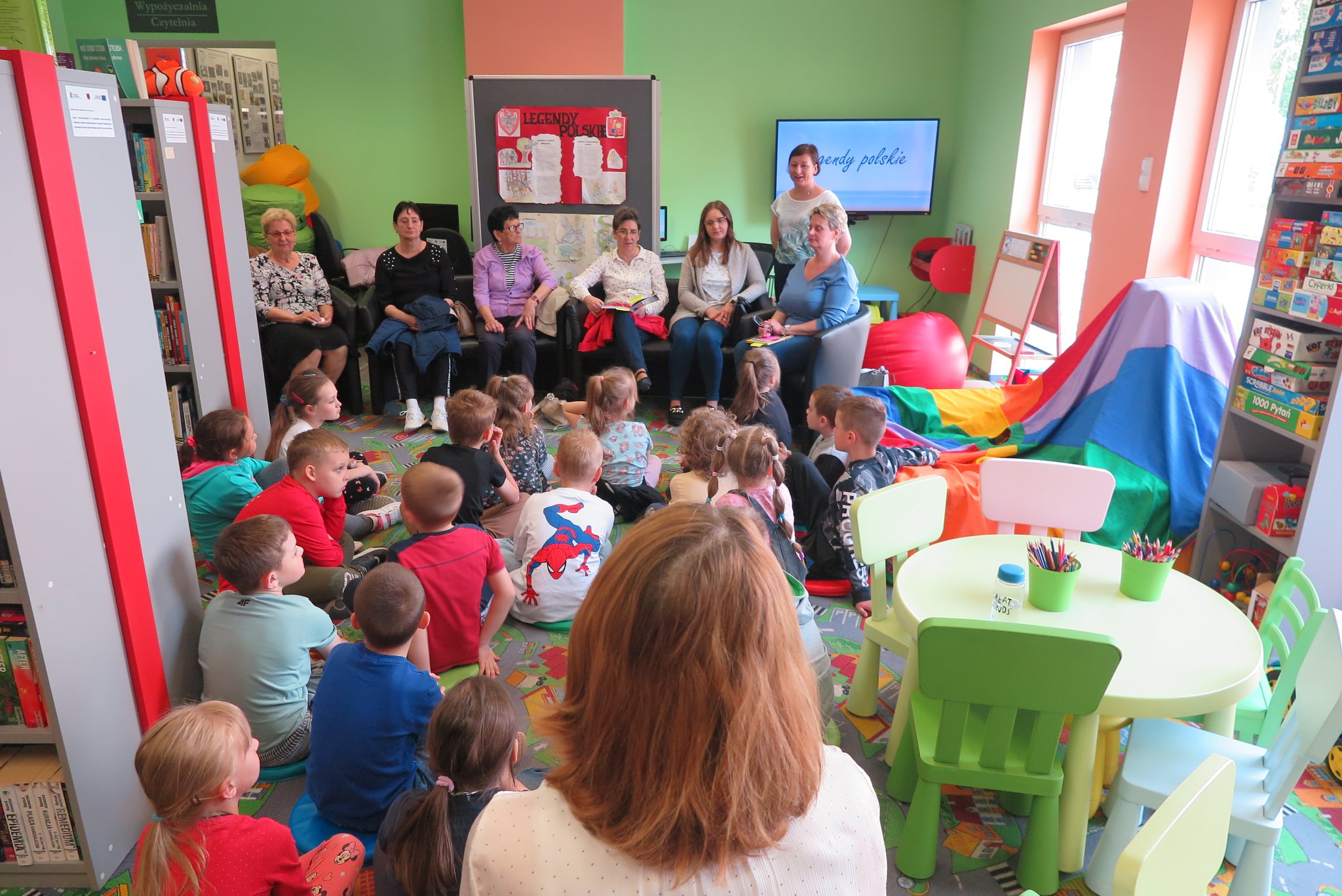 panie z domu seniora czytają polskie legendy uczniom  klasy 1b szkoły podstawowej nr 3  którzy siedzą na podłodze w oddziale dla dzieci