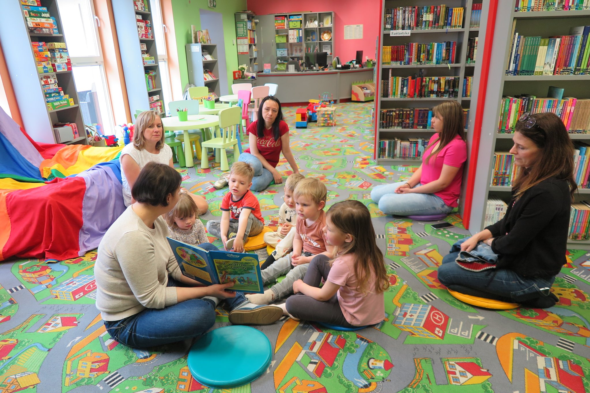 spotkanie klubu malucha, dzieci z rodzicami siedzą na podłodze w oddziale dla dzieci, bibliotekarka pokazuje im książkę