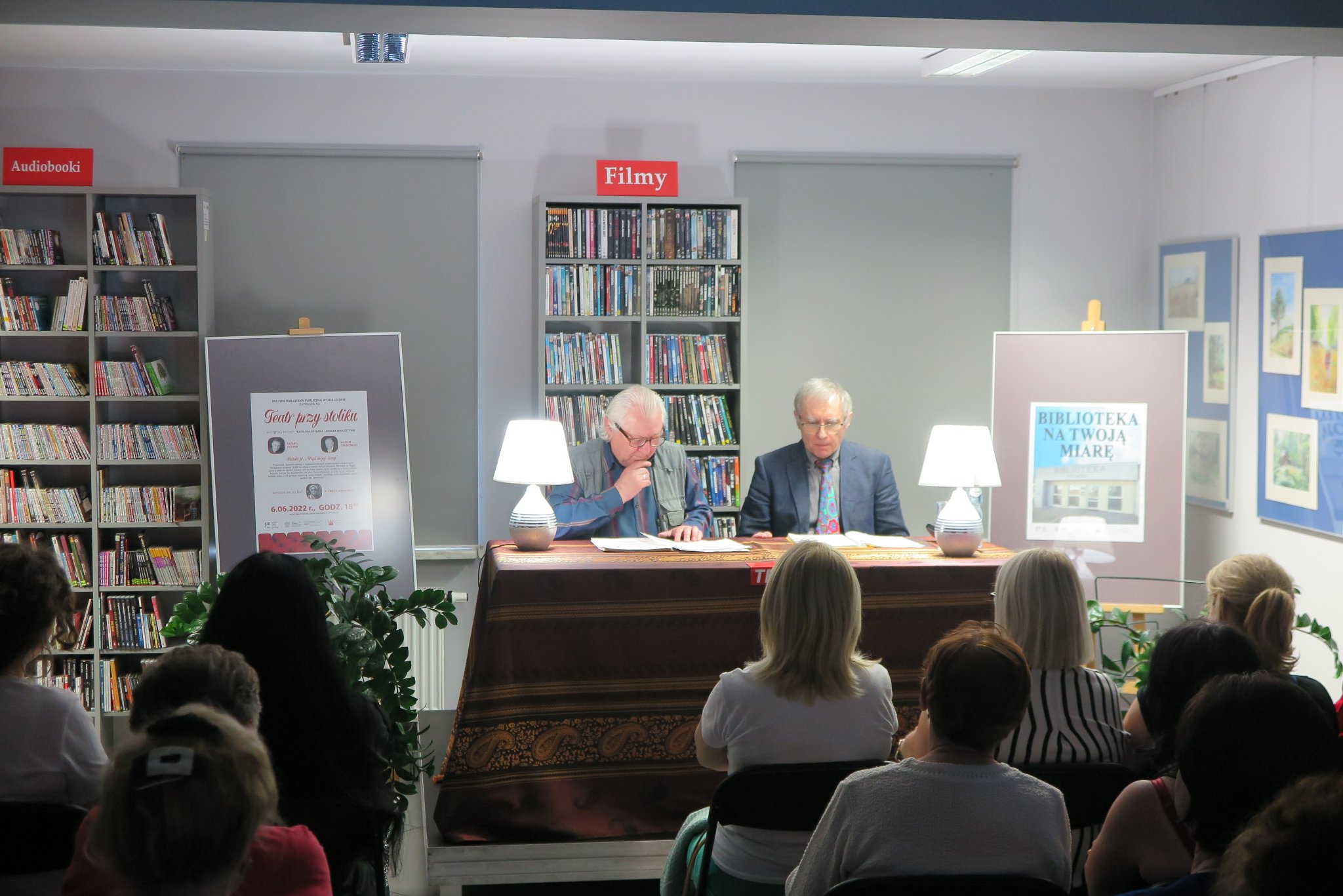 Cezary Ilczyna i Marian Czarkowski siedzą na krzesłach przy stoliku, przed nimi siedzi publiczność