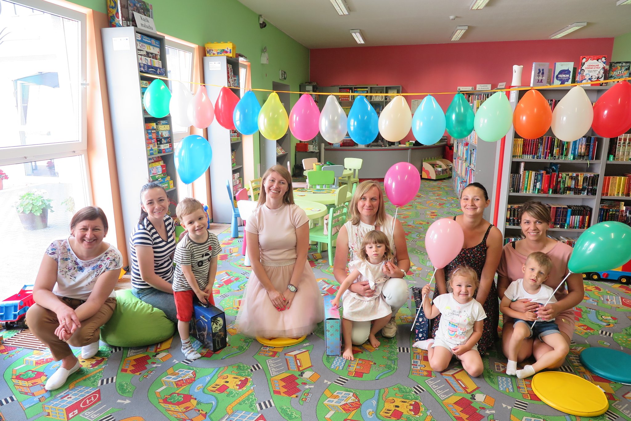 bibliotekarki i dzieci z rodzicami na grupowym zdjęciu, nad głowami wiszą balony