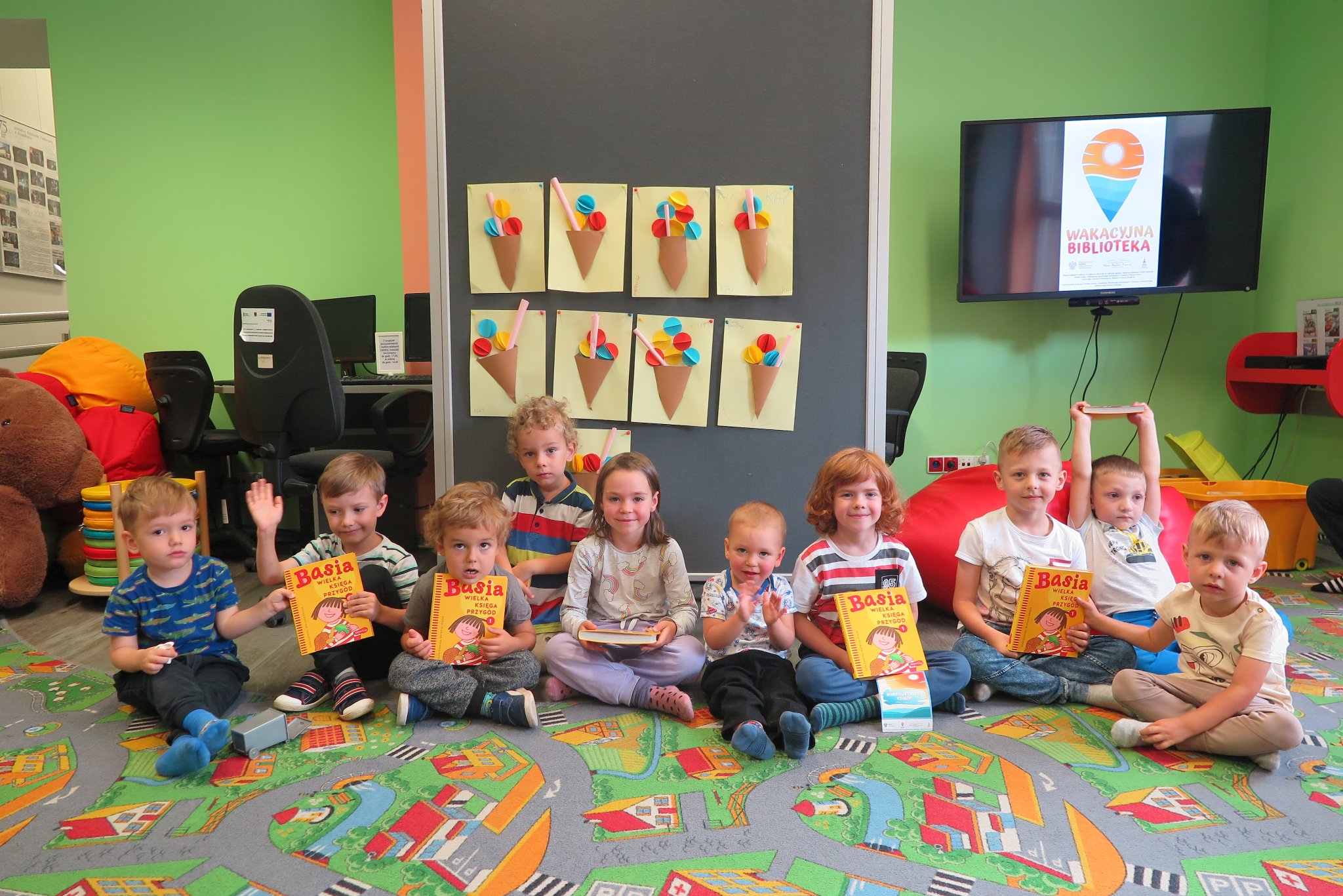 zdjęcie grupowe dzieci siedzących na podłodze w oddziale dla dzieci, część z nich trzyma w rękach książki