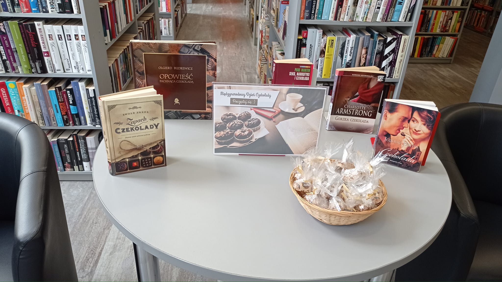 na stole leży koszyk z czekoladkami, obok stoją książki o tematyce czekolady lub z tytułem zawierającym czekoladę