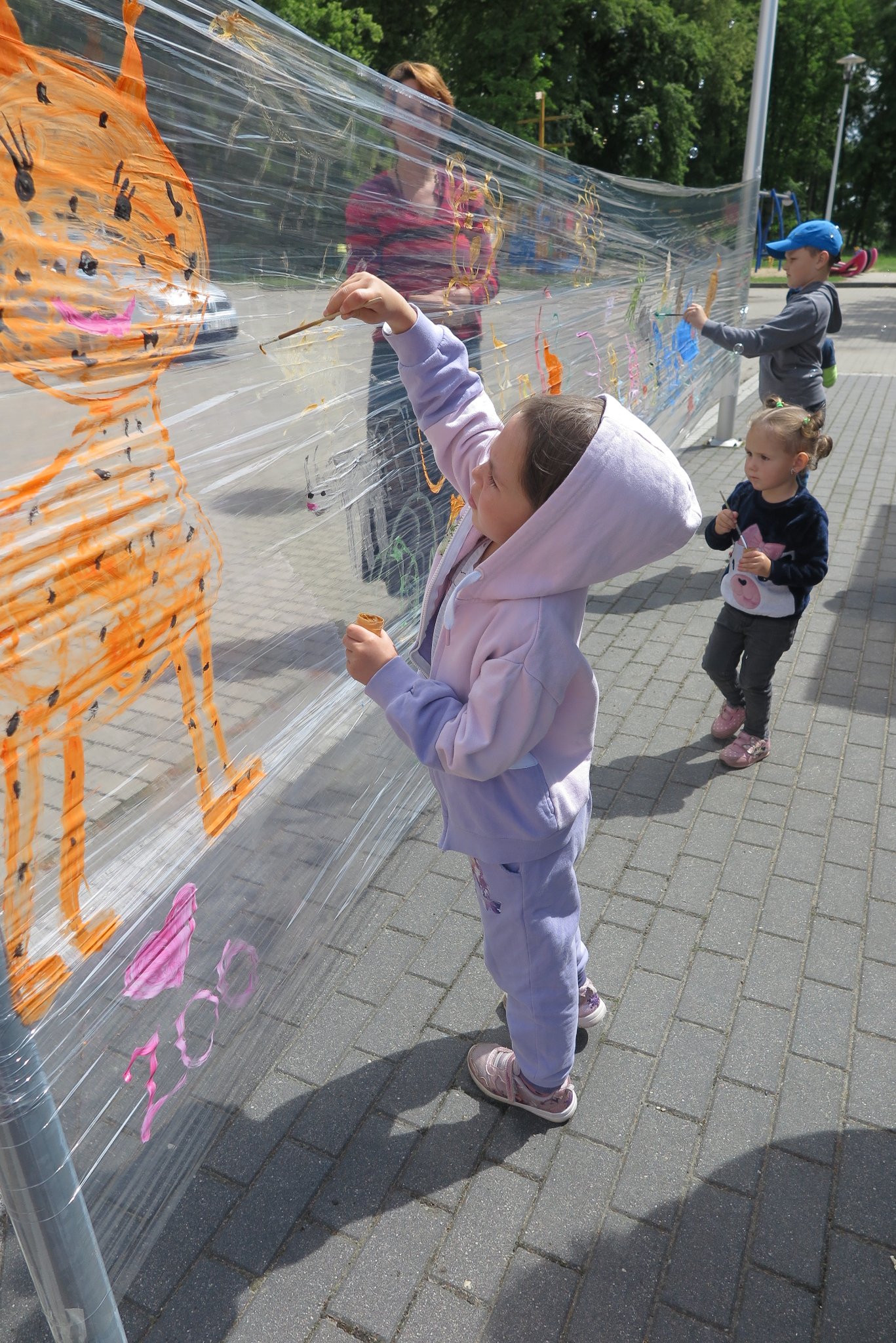 dzieci malują farbami na folii rozciągniętej między dwoma słupami
