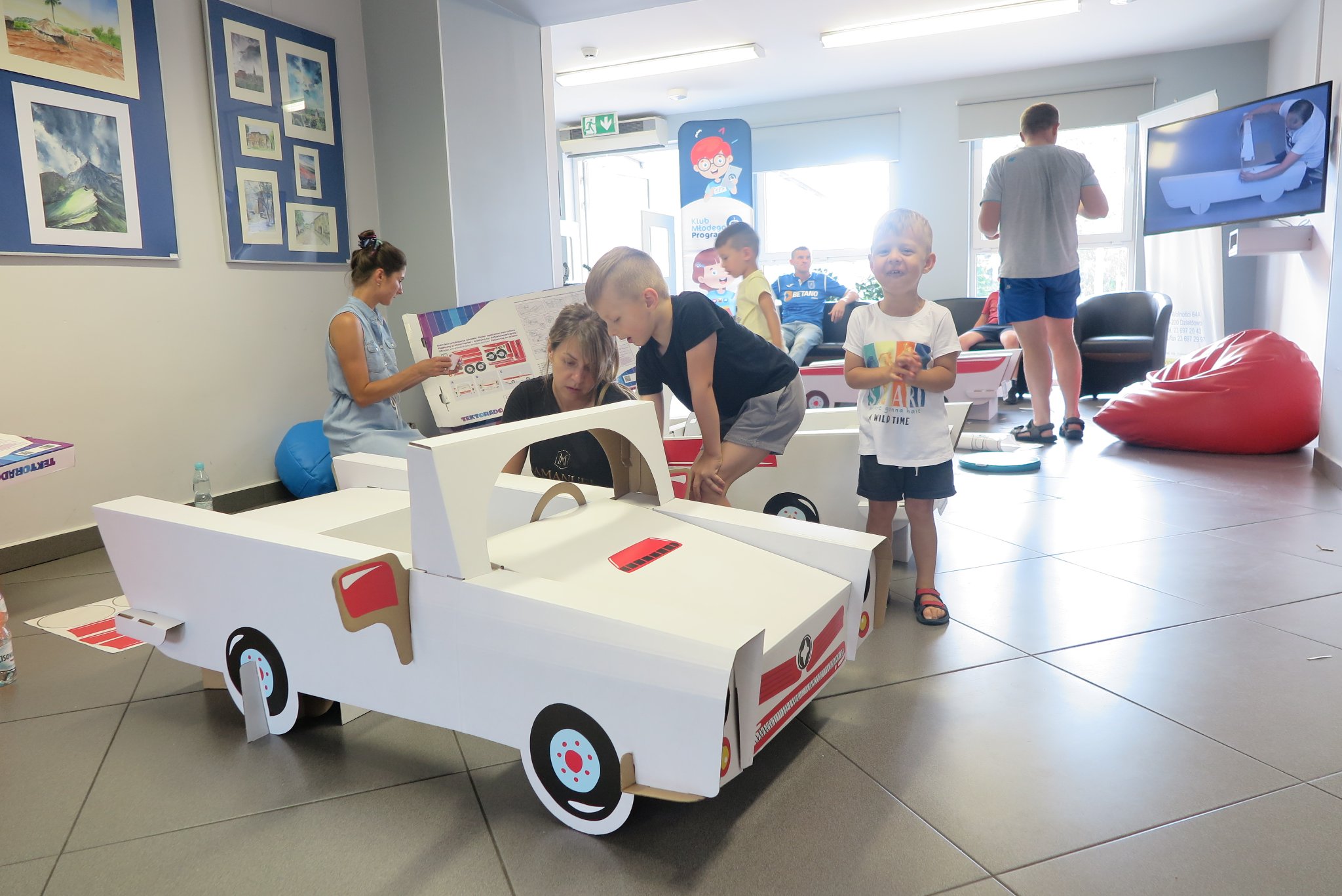 rodzice z dziećmi składają  tekturowy samochód w mediatece