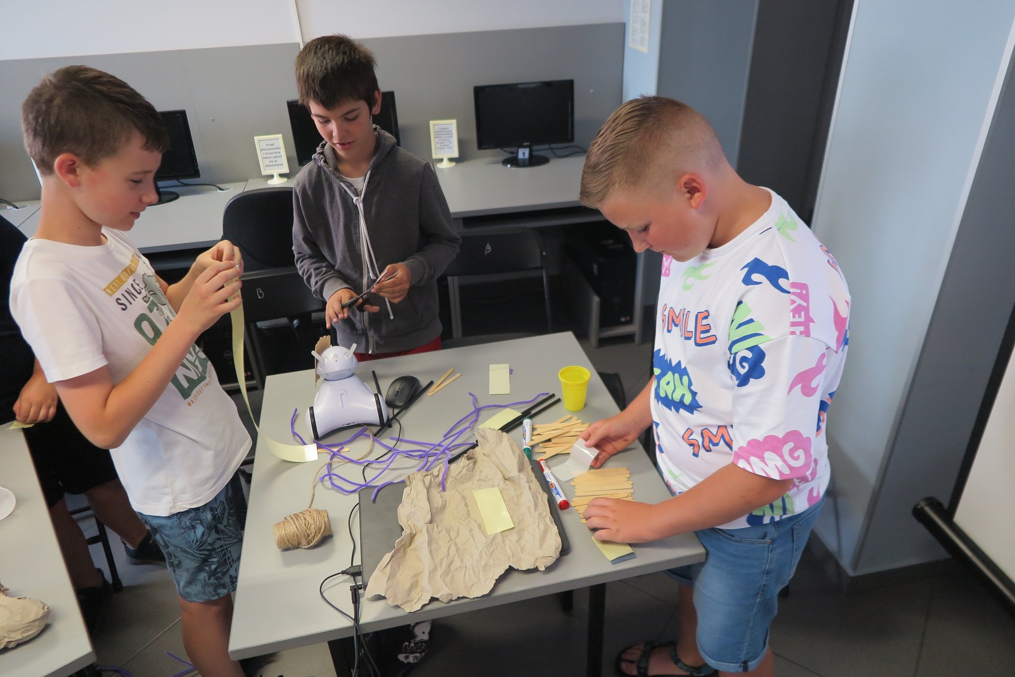 uczestnicy klubu młodego programisty customizują roboty oklejając je papierem, patyczkami po ladach, słonkami i sznurkiem