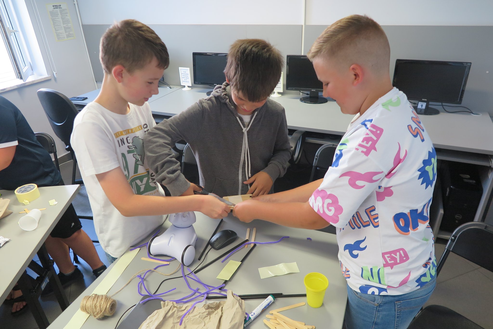 uczestnicy klubu młodego programisty customizują roboty oklejając je papierem, patyczkami po ladach, słonkami i sznurkiem