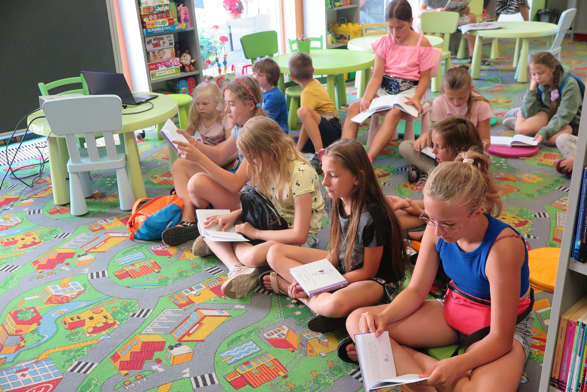 uczestnicy Wakacyjnego Klubu Książki siedzą na podłodze na kolorowych okrągłych poduszkach, każdy trzyma swoją książkę
