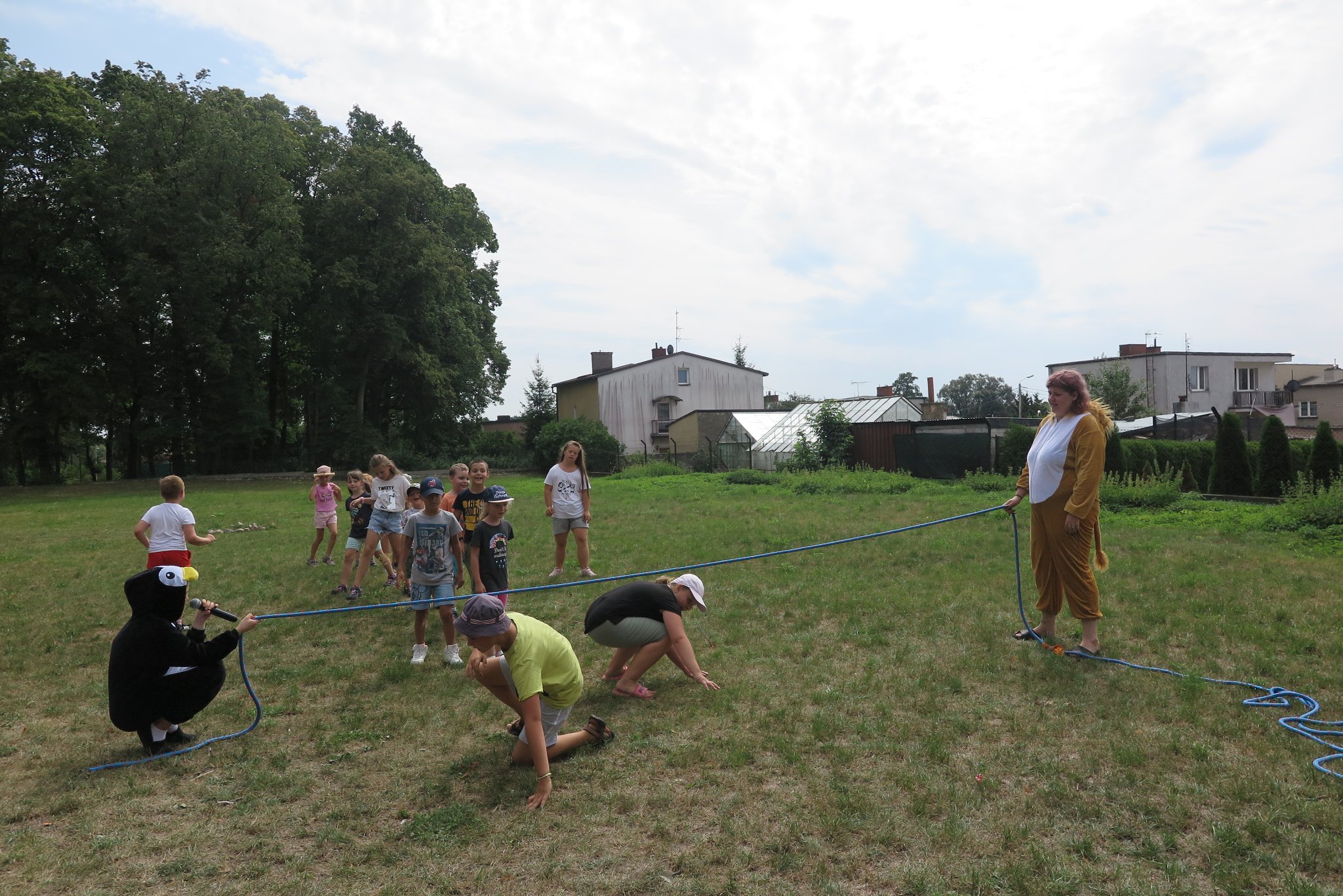 aktorzy stoją na trawie, trzymając rozciągniętą skakankę pod którą przechodzą dzieci