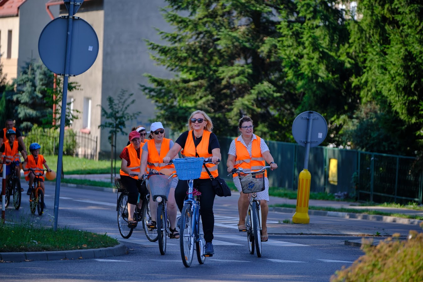 uczestnicy rajdu rowerowego jadą drogą publiczną (rondo), wszyscy mają założone pomarańczowe kamizelki odblaskowe z napisem Odjazdowy Bibliotekarz