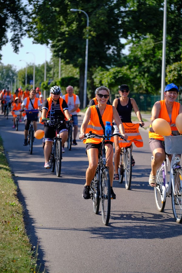 uczestnicy rajdu rowerowego jadą drogą publiczną, wszyscy mają założone pomarańczowe kamizelki odblaskowe z napisem Odjazdowy Bibliotekarz