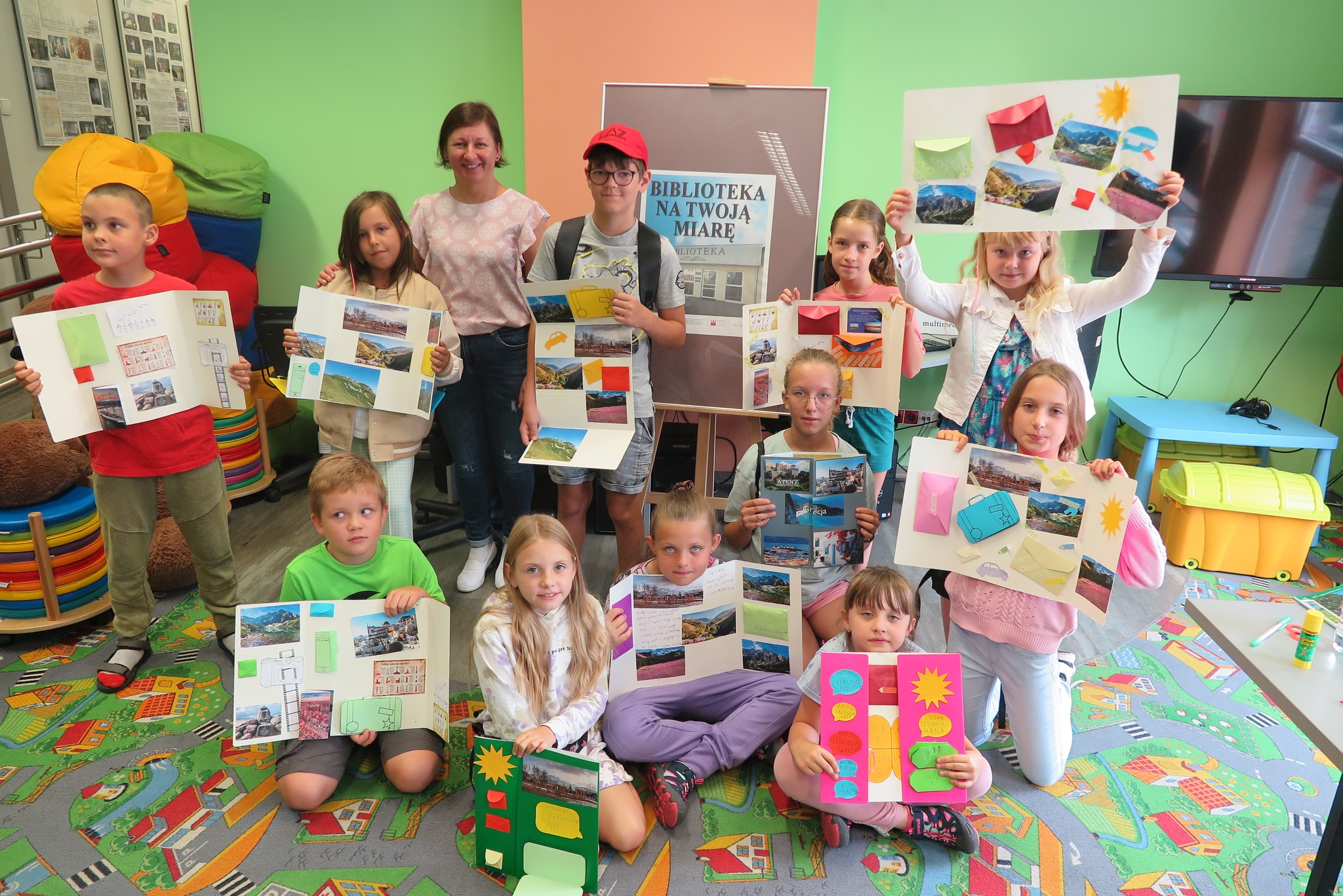 dzieci pokazują wykonane lapbooki, obok na podłodze stoi plakat Blisko