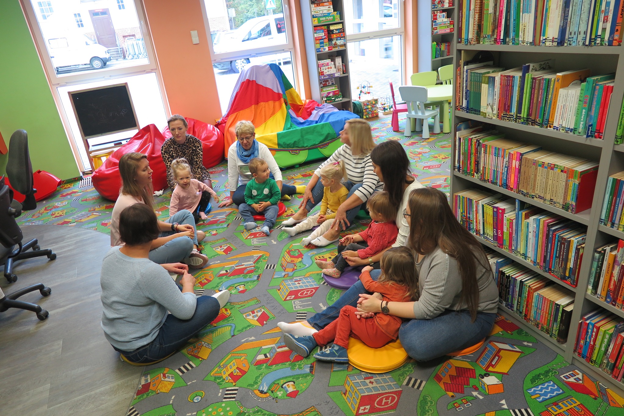 dzieci z rodzicem siedzą na dywanie w oddziele dla dzieci z bibliotekarkami