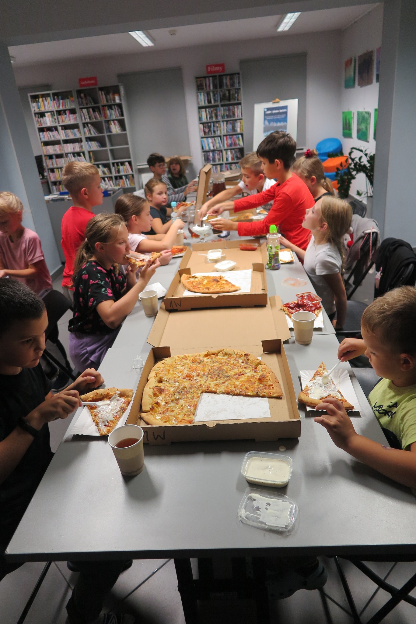 dzieci jedzą pizzę przy stole w mediatece