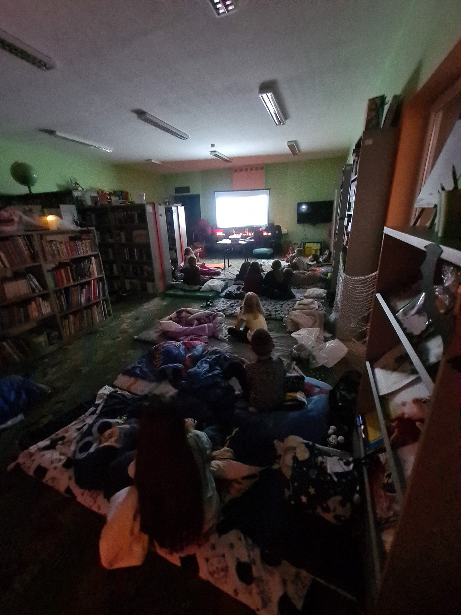 dzieci leżą na materacach w oddziale dla dzieci i oglądają film na ekranie projektora przy zgaszonym świetle