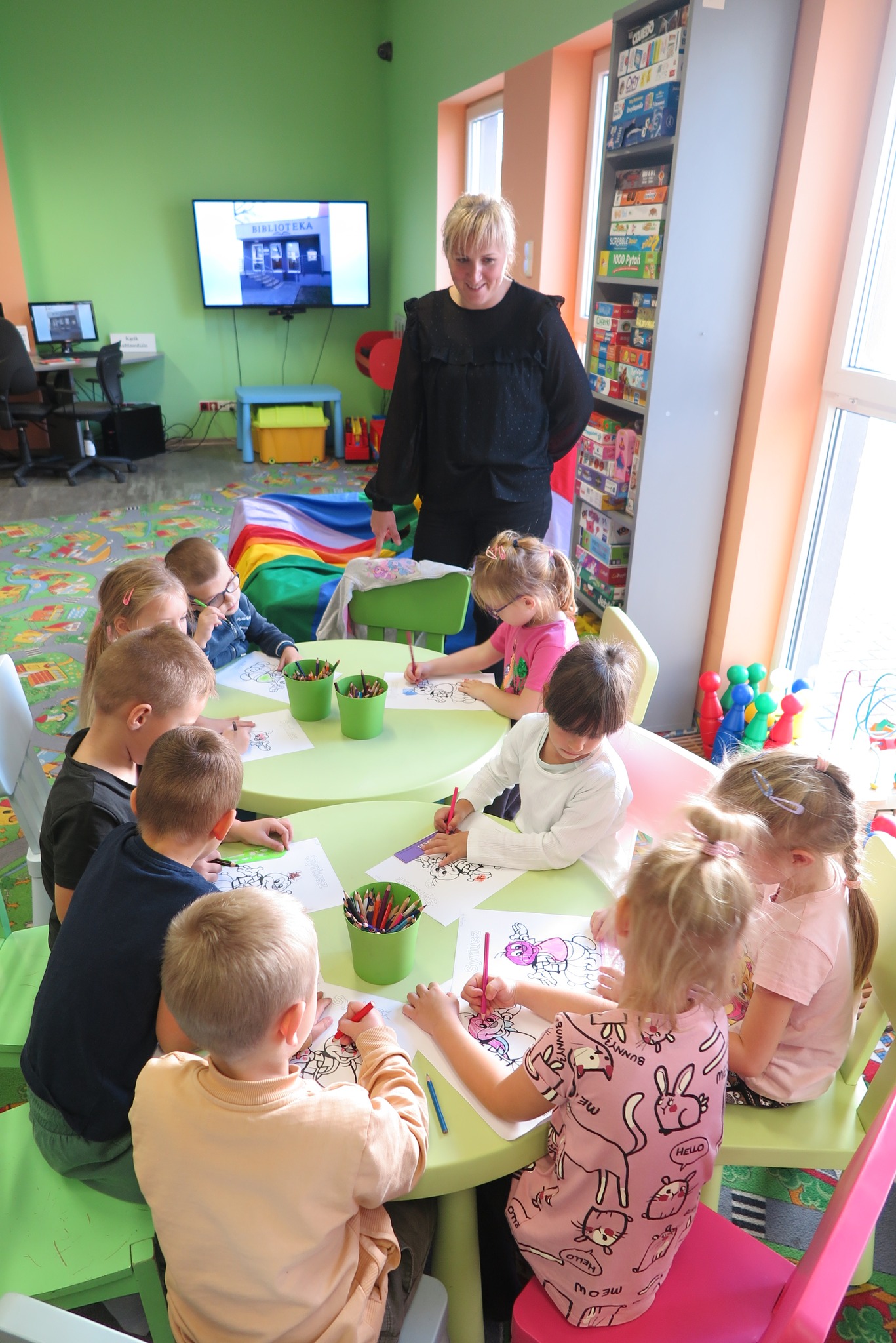 dzieci siedzą w oddziale dla dzieci przy stolikach i kolorują obrazki