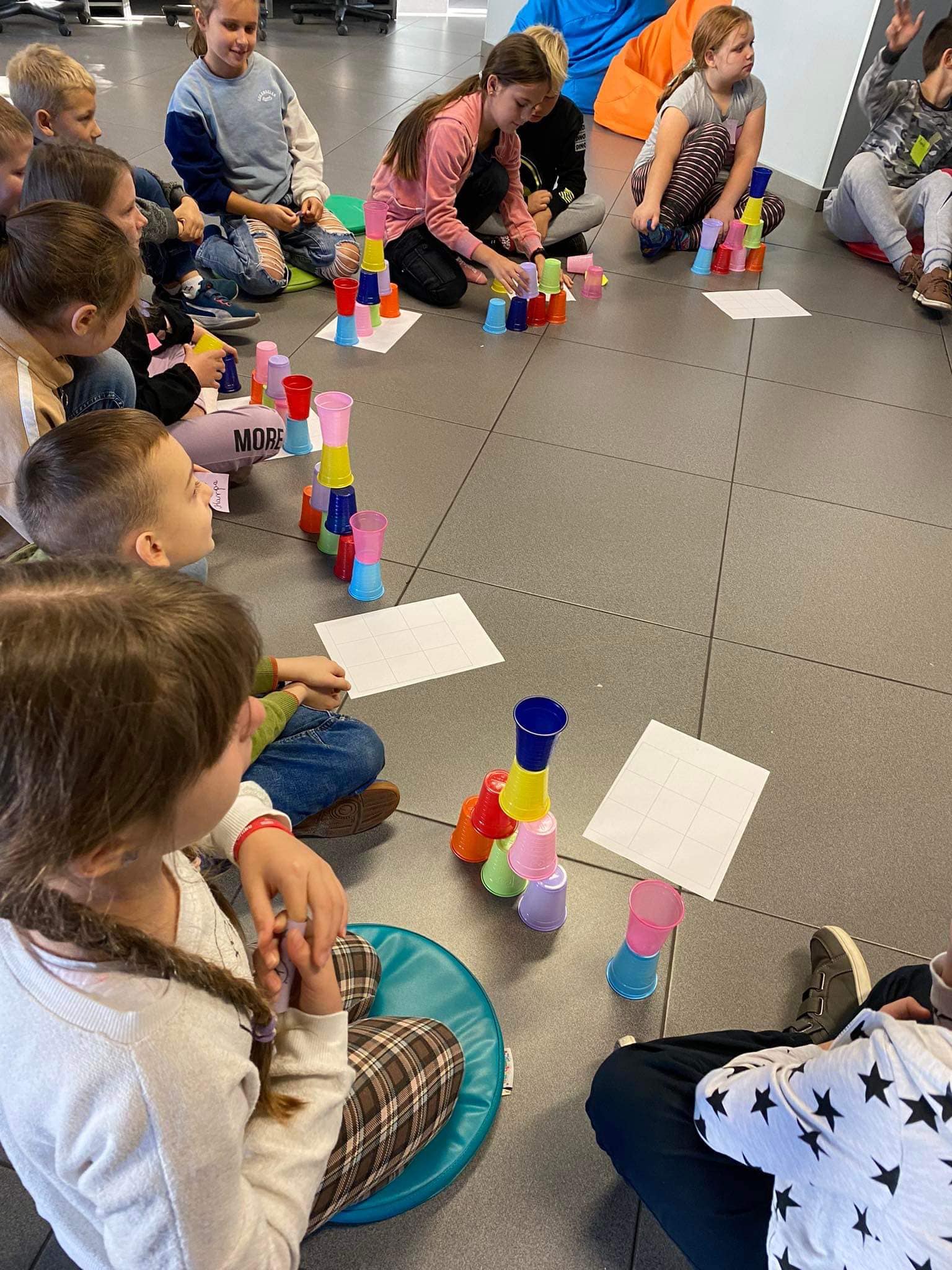 dzieci siedzą w kółku w MEDIATECE, układają piramidę z kolorowych kubków