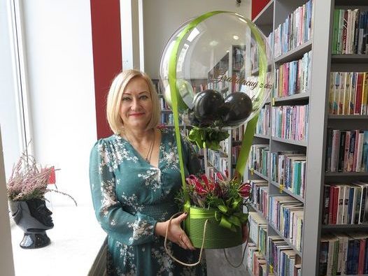 dyrektor biblioteki trzyma w rękach kwiaty z balonem od pracowników biblioteki za 20 lecie pracy