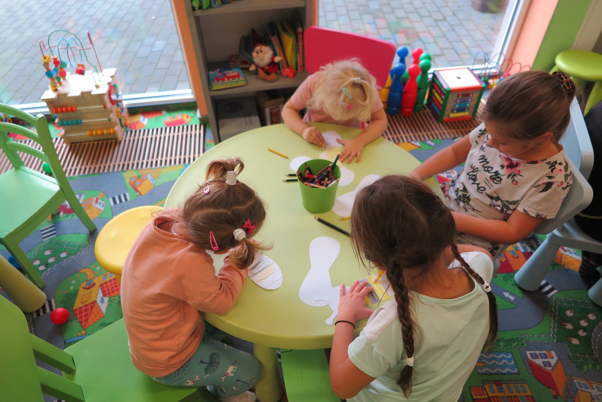 dzieci siedzą przy okrągłych stolikach i kolorują wycięte z papieru pszczoły