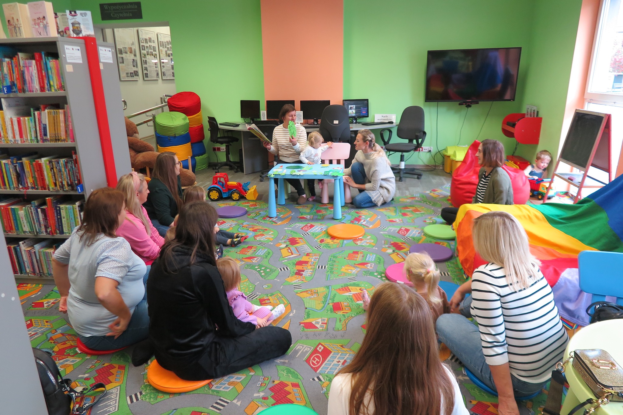 uczestnicy klubu malucha słuchają czytanej książki siedząc na dywanie w oddziale dla dzieci