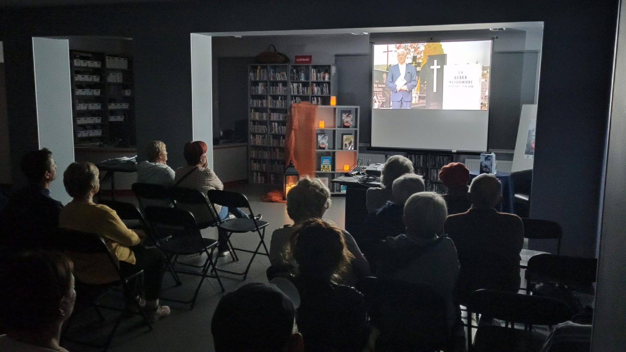 na ekranie projektora puszczany jest film, publiczność siedzi w ciemnej sali