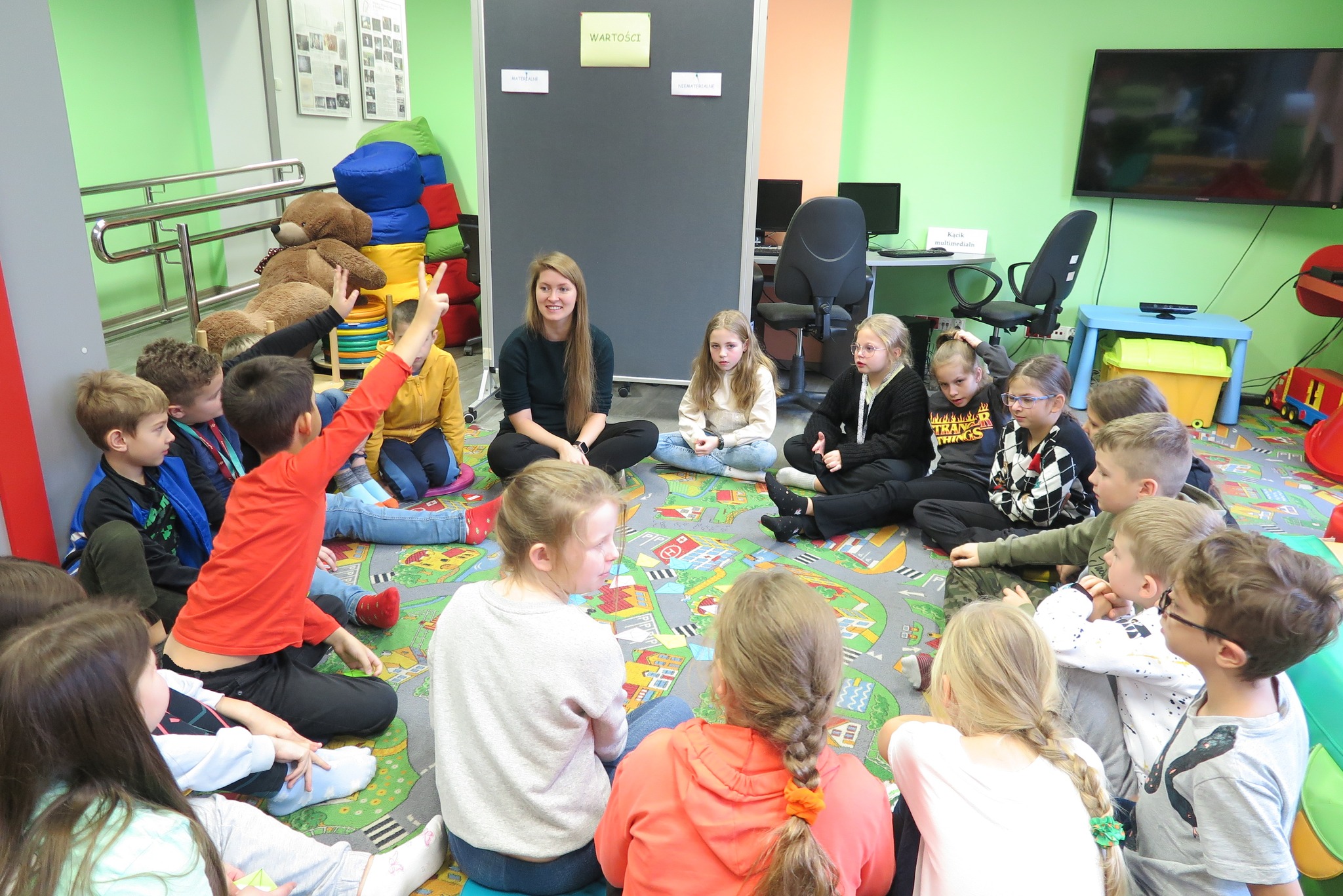 uczniowie i bibliotekarka siedzą w kole na dywanie w oddziale dla dzieci