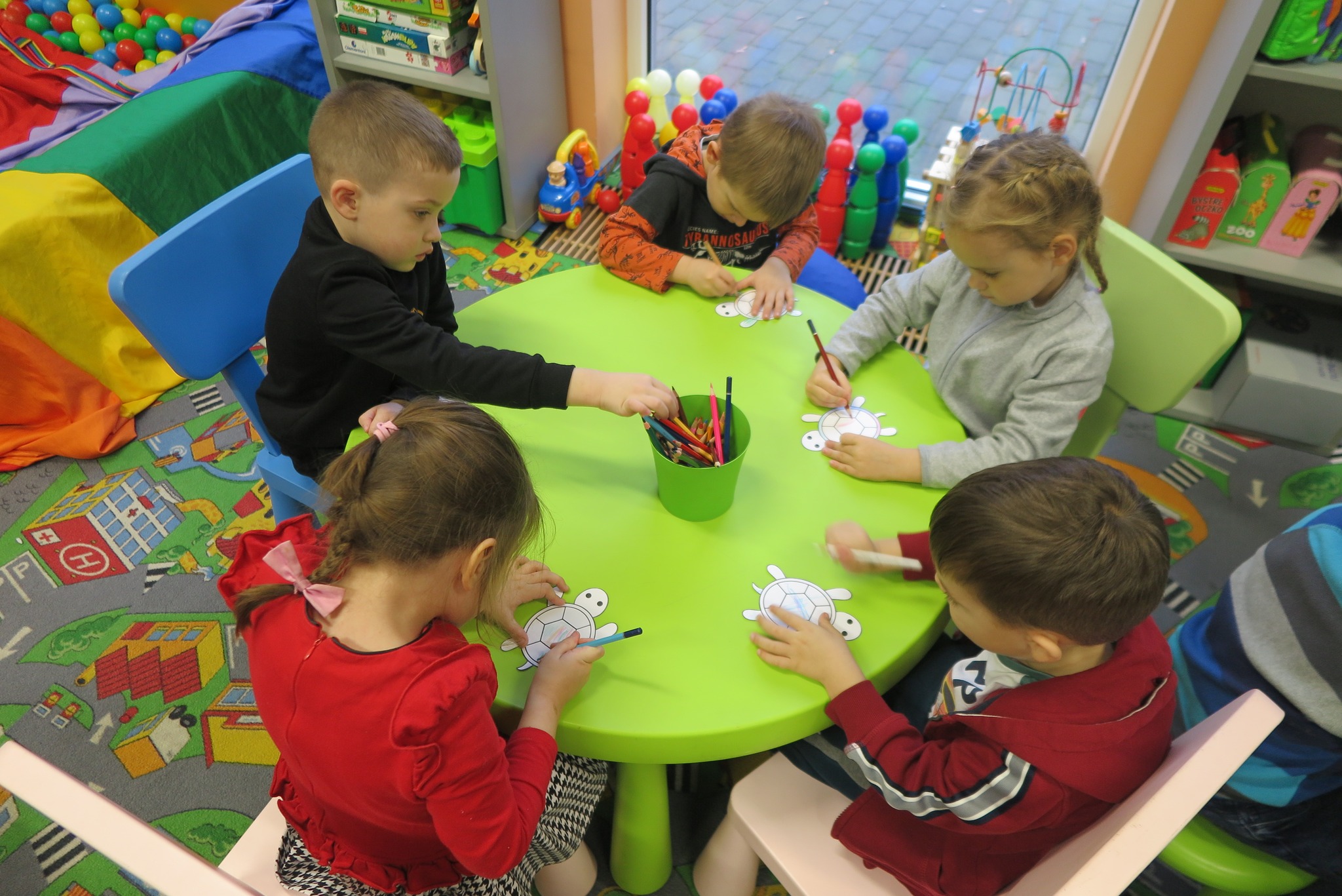 dzieci kolorują wycinankę siedząc przy okrągłym stoliku 